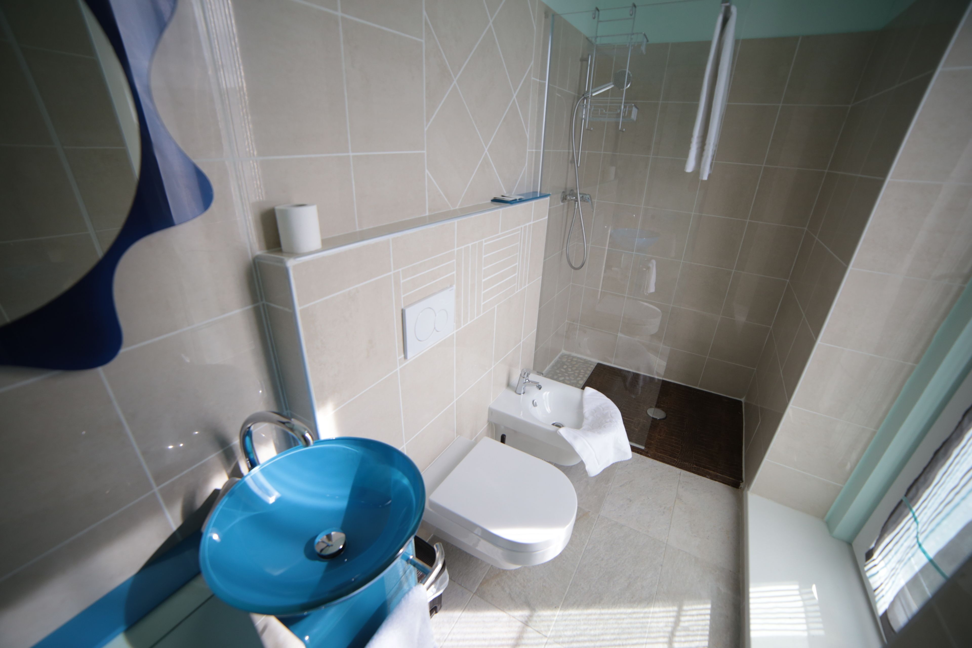 Une salle de bain moderne avec un lavabo bleu, des toilettes blanches et une douche à parois de verre.