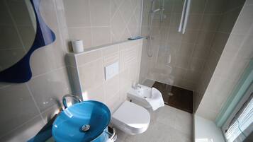 Une salle de bain moderne avec un lavabo bleu, des toilettes blanches et une douche à parois de verre.
