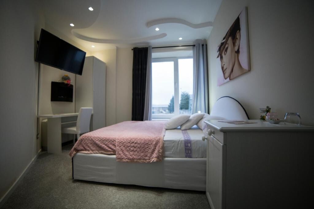 A bedroom with a bed, a desk, a TV, and a window.