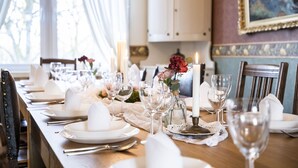 A dining table set with white plates, glasses, and candles, featuring a vase with red flowers. - Skotteks Gården (Ulricehamn)