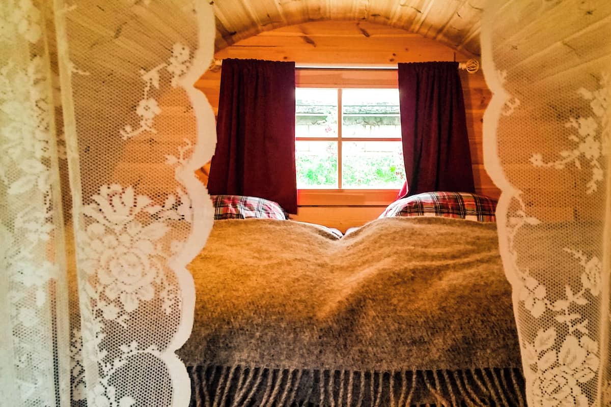 A room with a bed, lace curtains, and a window with a view of greenery.