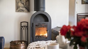 A cozy room with a wood-burning stove, a coffee table with a cup, and a decorative vase. - Skotteks Gården (Ulricehamn)