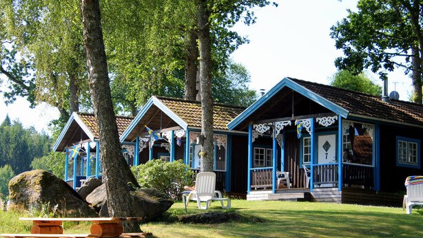 A row of cabins with a picnic table in front, surrounded by trees and a grassy area. - Skotteks Gården (Ulricehamn)