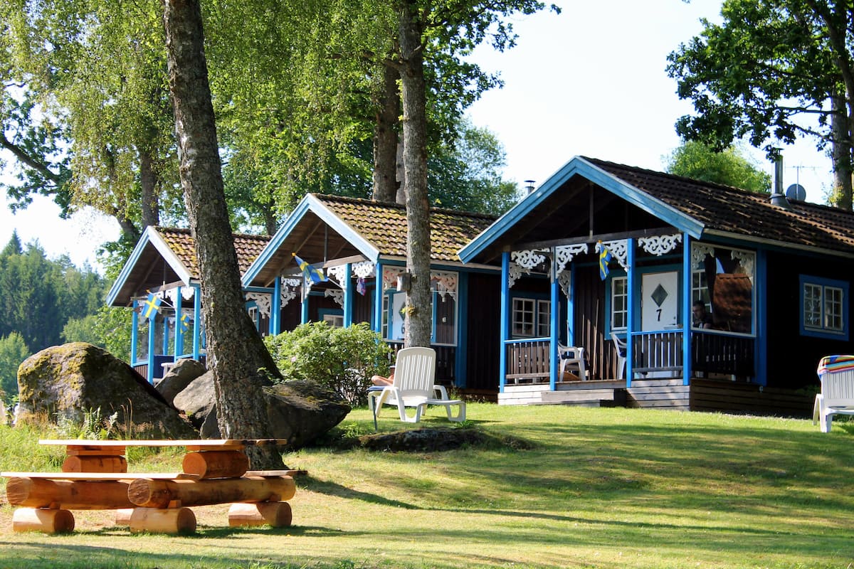 A row of cabins with a picnic table in front, surrounded by trees and a grassy area.