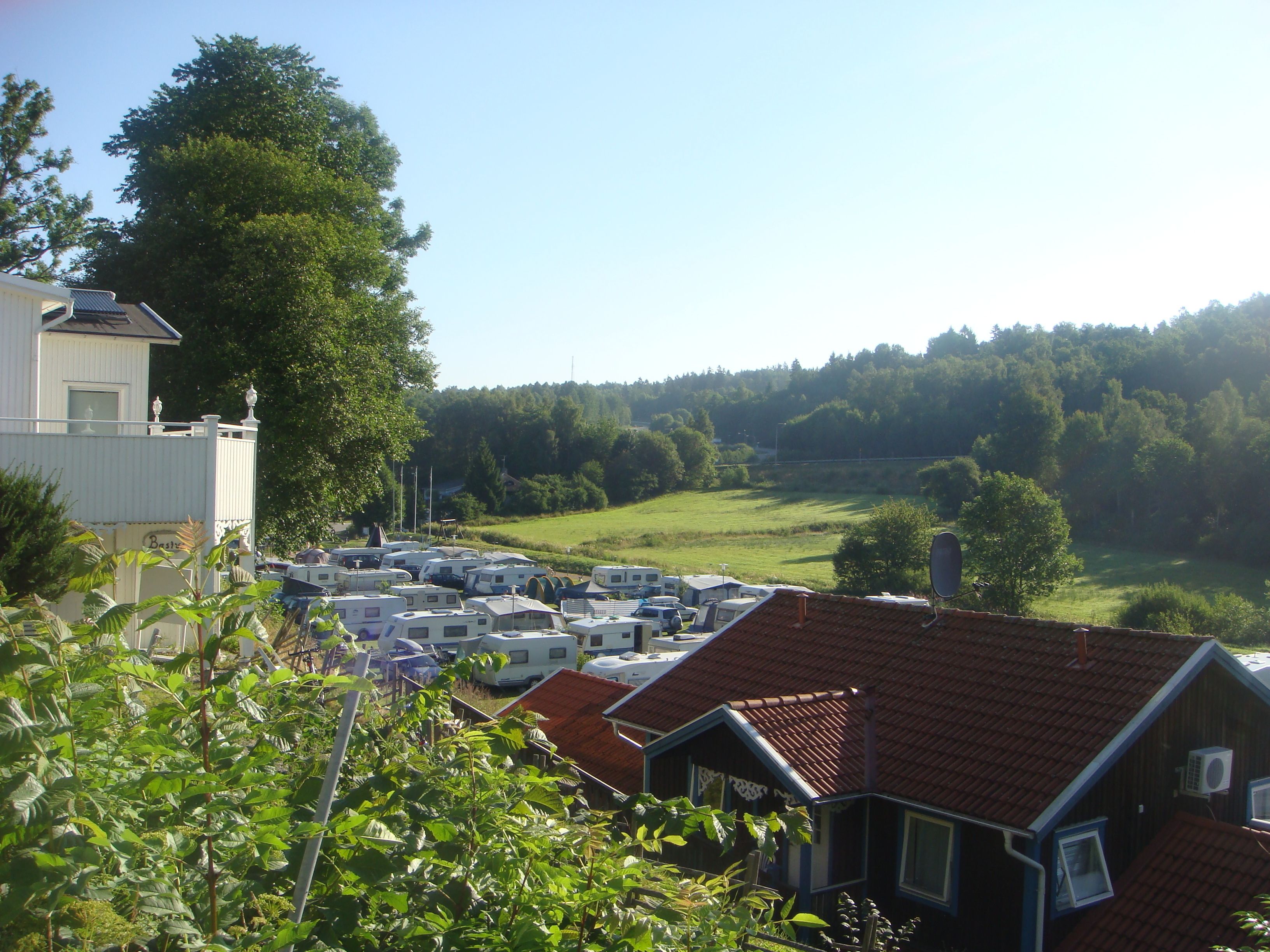 A campground with RVs parked in rows, surrounded by trees and a building with a red roof.