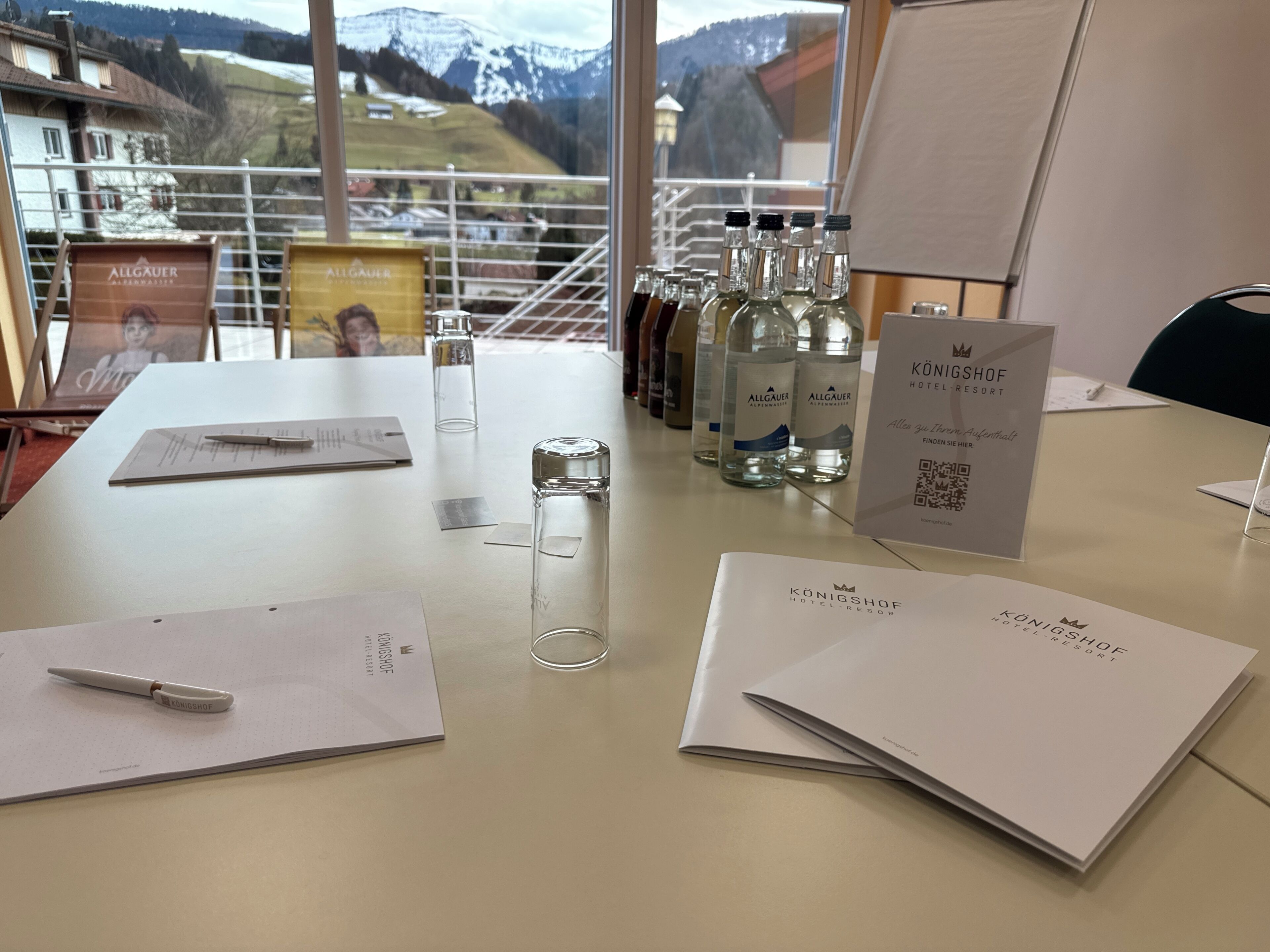 A hotel desk with a view of mountains, a pen, papers, and water bottles.