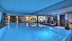 A large indoor swimming pool with a stone wall and lounge chairs. - Königshof Hotel Resort- Partner von Oberstaufen PLUS und PLUS GOLF (Oberstaufen)
