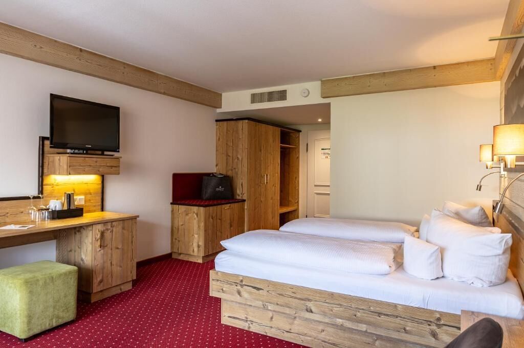 Habitación de hotel con una cama de madera, un escritorio con televisor, un armario y una alfombra roja.