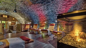 A spa room with wooden flooring, multiple sun loungers, a stone wall, and a glass enclosure with a rock display. - Königshof Hotel Resort- Partner von Oberstaufen PLUS und PLUS GOLF (Oberstaufen)