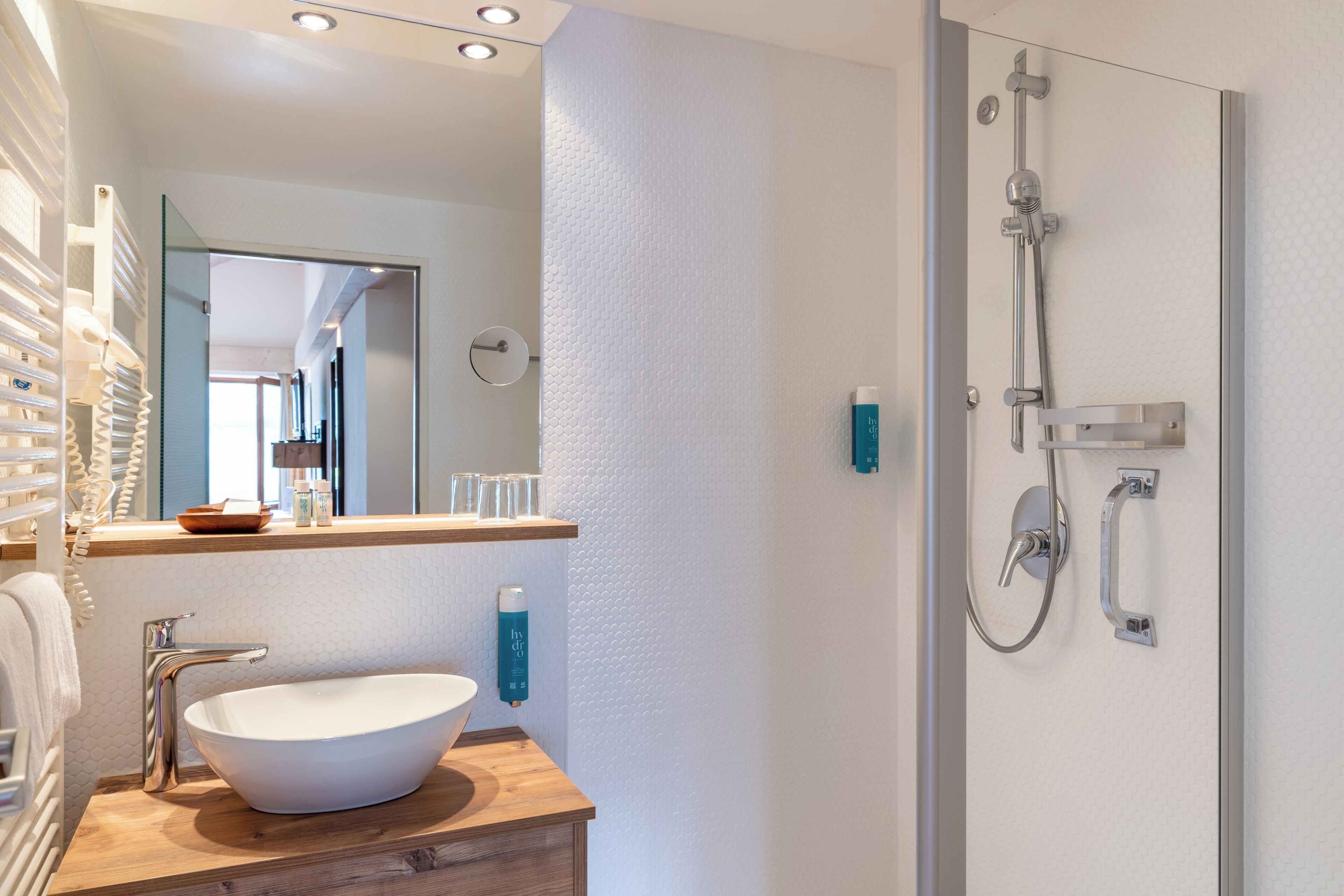 A modern bathroom with a large white vessel sink, a handheld showerhead, and a glass-enclosed shower.