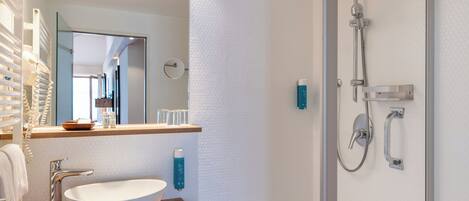 Un baño moderno con un lavabo blanco de diseño, un cabezal de ducha de mano y una ducha con mampara de vidrio.
