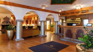 A hotel lobby with wooden beams, a reception desk, and a large potted plant. - Königshof Hotel Resort- Partner von Oberstaufen PLUS und PLUS GOLF (Oberstaufen)