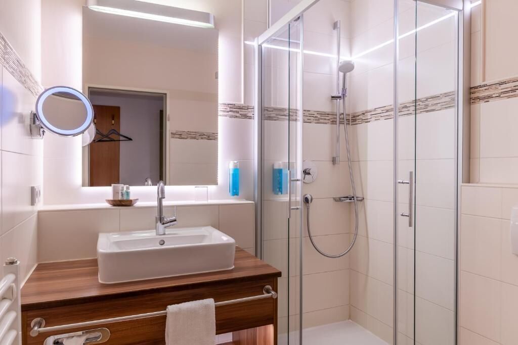 A modern bathroom with a rectangular sink, a glass shower enclosure, and a mirror with a ring light.