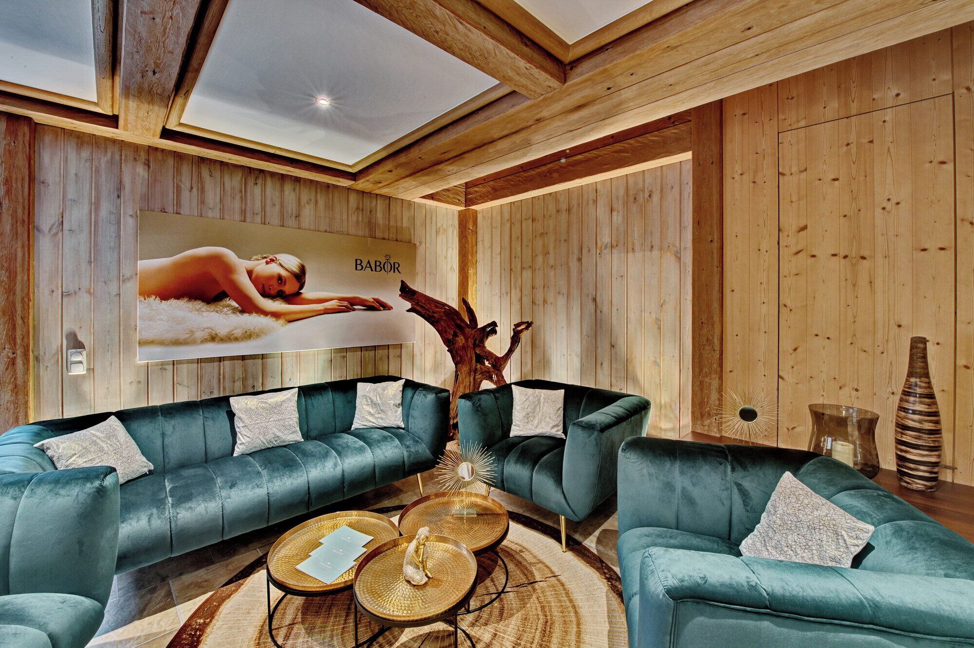 A modern interior with wooden panel walls, a large ceiling skylight, and two teal sofas with white pillows.
