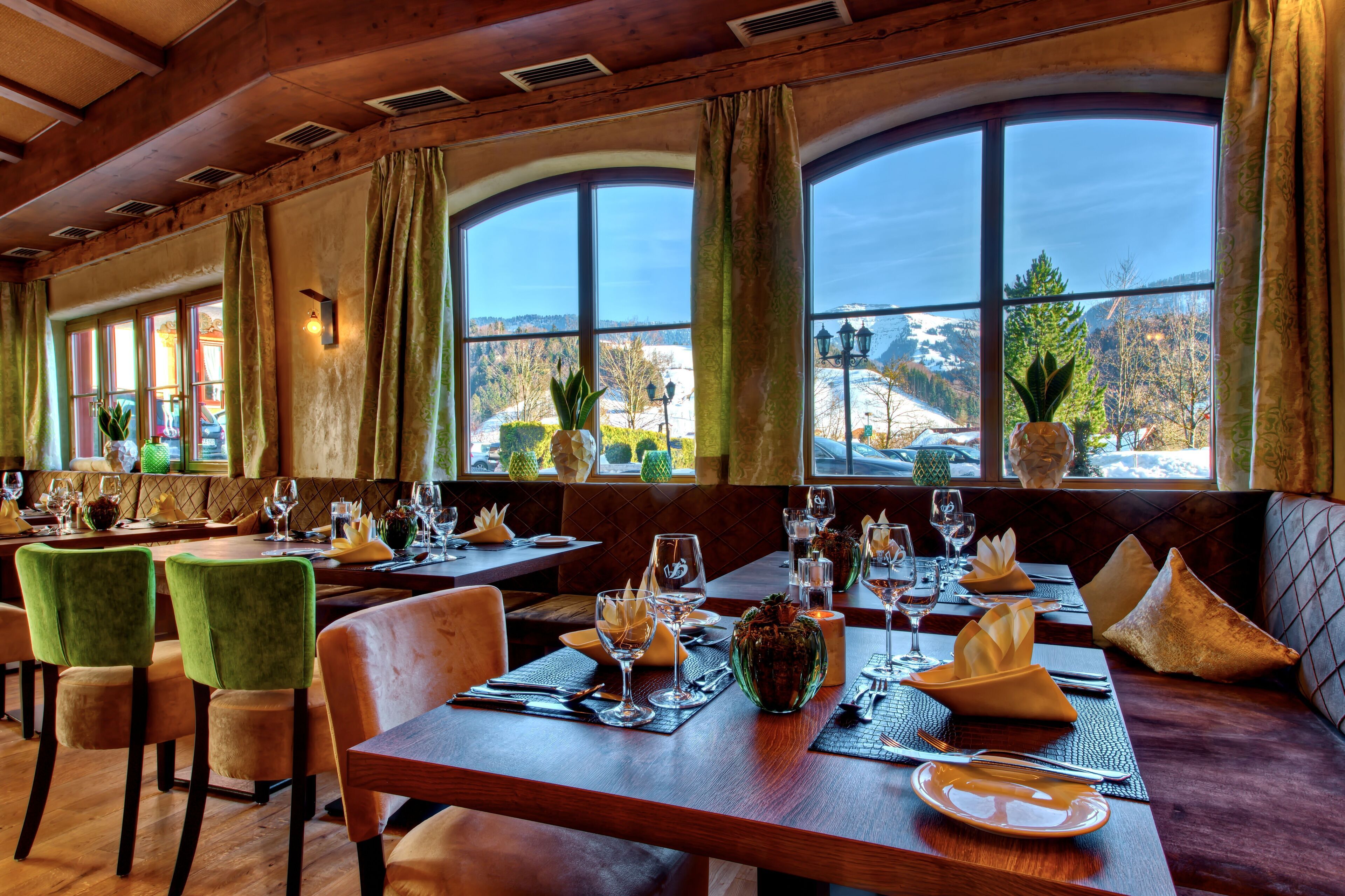 Ein Restaurant mit Holztischen, grünen Stühlen und großen Fenstern mit Blick auf eine verschneite Landschaft.
