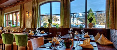 Un restaurante con mesas de madera, sillas verdes y amplios ventanales que ofrecen vistas a un paisaje nevado.