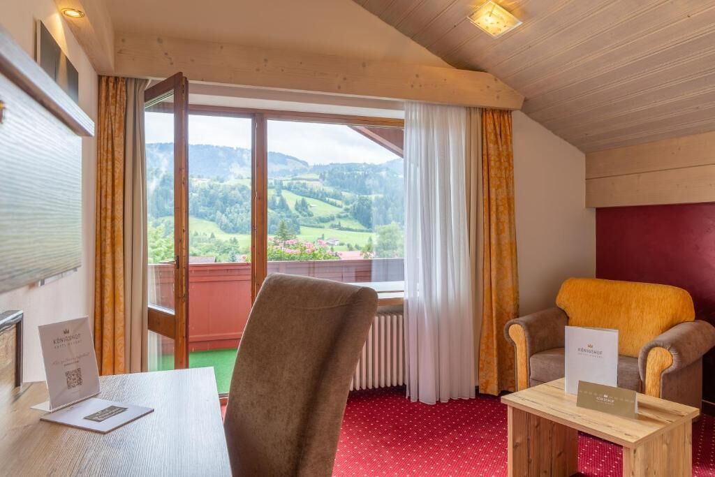 Een kamer met uitzicht op een groen landschap, een houten tafel, twee stoelen en een rood tapijt.