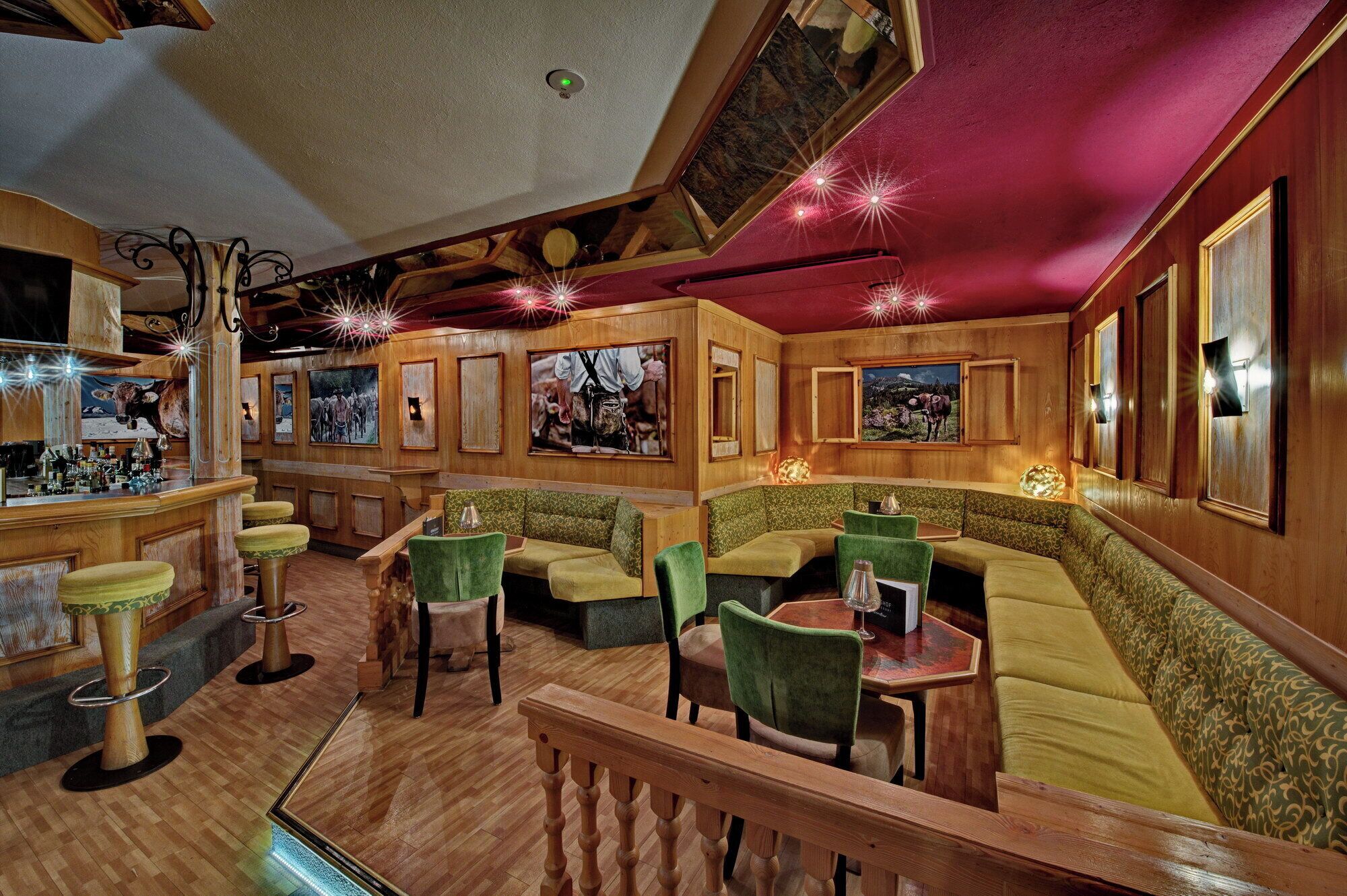 A bar area with wooden walls, green cushioned seating, and a bar counter with bottles.