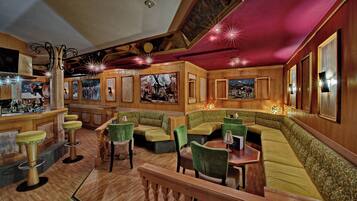 A bar area with wooden walls, green cushioned seating, and a bar counter with bottles.