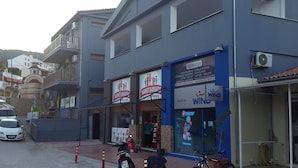 A building with a blue facade, a sign for 'MARKET DIAMANTIC', and a 'WIND' sign. There are parked cars and a motorcycle in front. - Pension Pineapple (Skiathos)