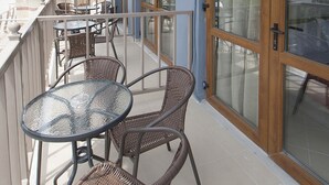 A balcony with wicker chairs and a glass table, overlooking a street with buildings and a red-roofed structure. - Pension Pineapple (Skiathos)