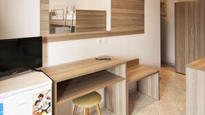 A modern, well-lit room with a wooden desk, a chair, a television, and a refrigerator. - Pension Pineapple (Skiathos)