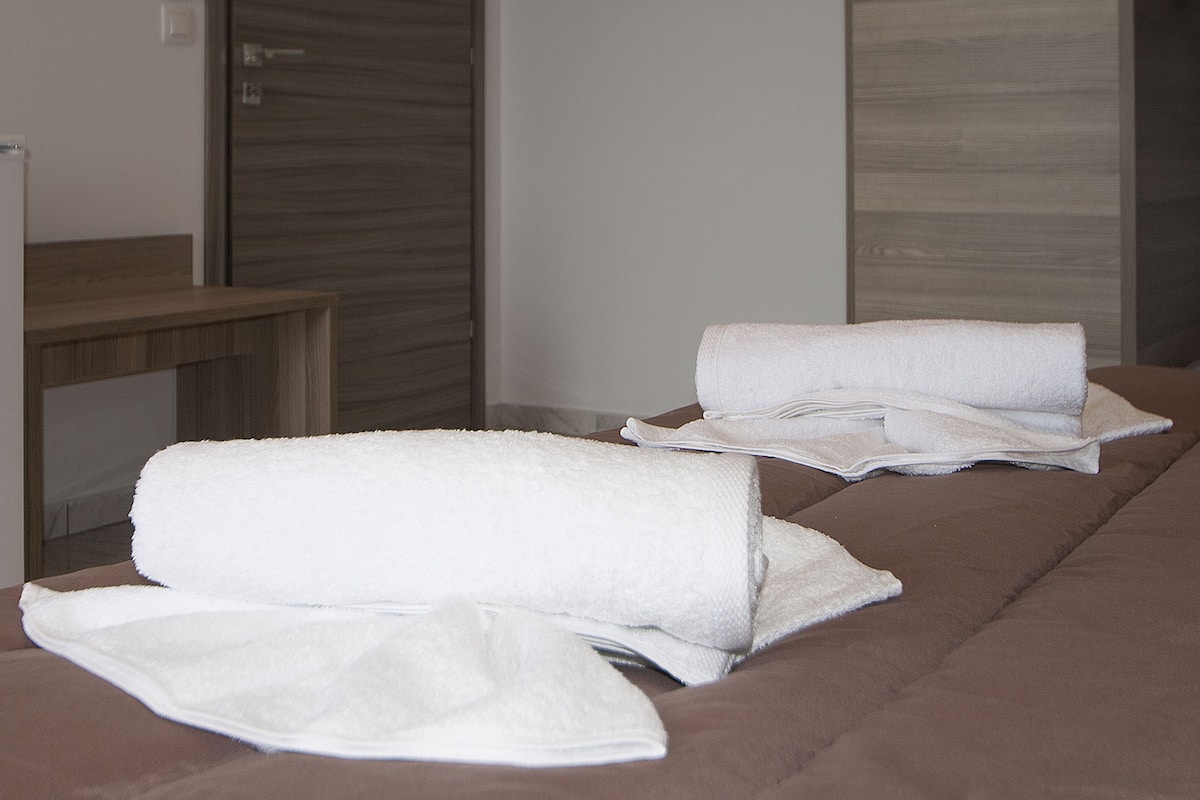 A hotel room with a bed, a wooden nightstand, and a mirror.