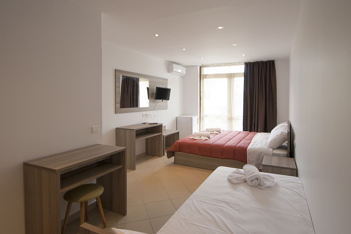 A hotel room with a bed, a desk, a chair, a TV, and a window with curtains.