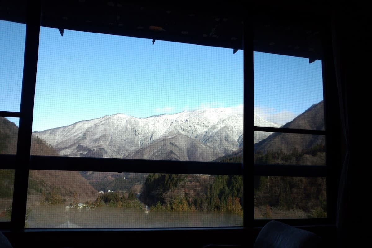 A view from a window with a mountain landscape, including snow-capped peaks and a lake.