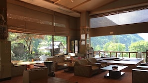 A spacious living area with large windows, a sofa, a coffee table, and a fireplace. - Ryokan Sansui (Takayama)