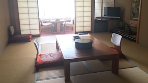 A traditional Japanese-style room with tatami flooring, a low table with cushions, a television, and sliding doors. - Ryokan Sansui (Takayama)