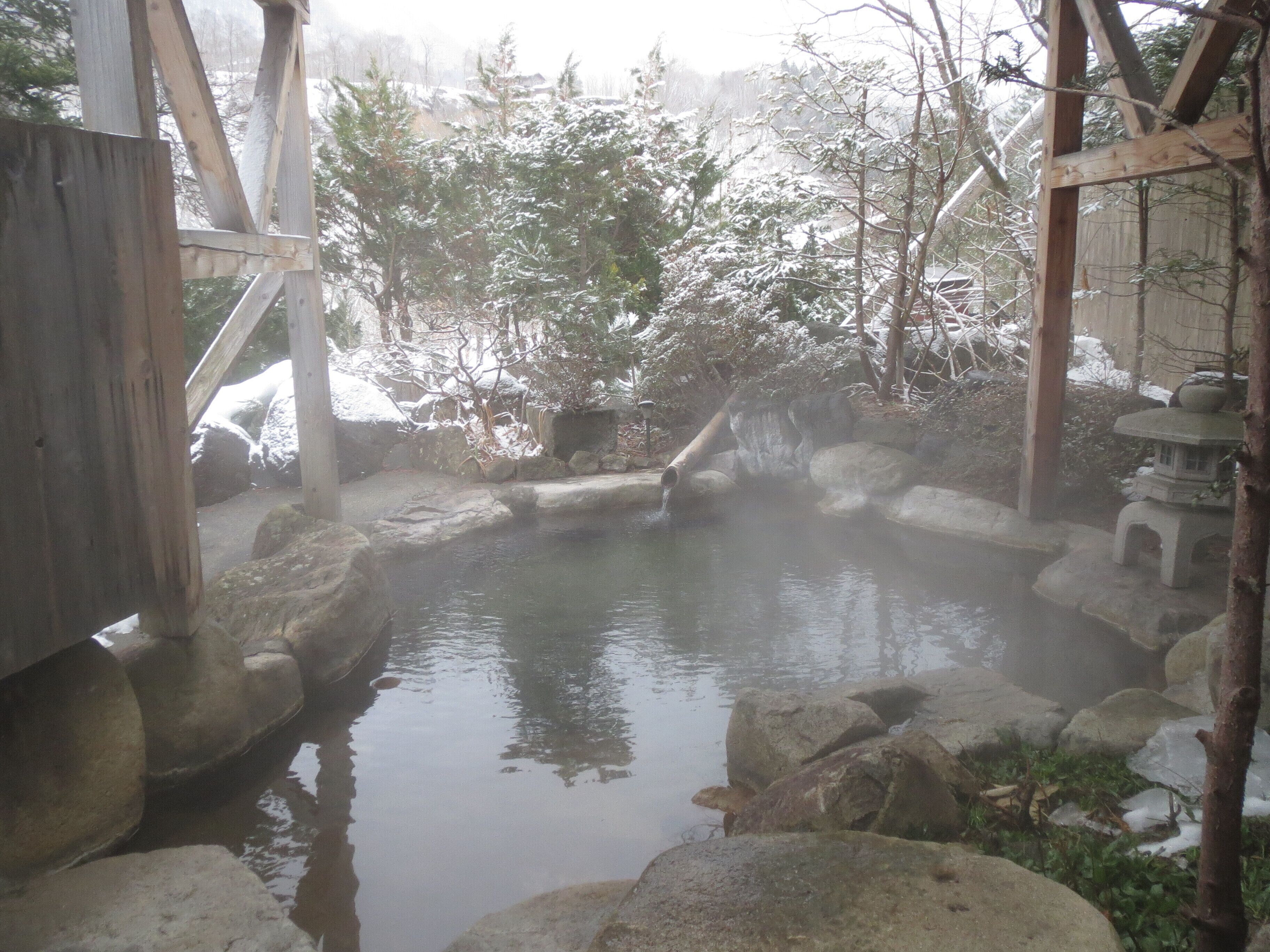 A traditional Japanese onsen with a stone bath surrounded by rocks and a wooden structure.