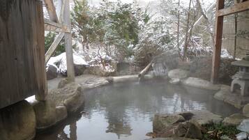 A traditional Japanese onsen with a wooden structure, a stone bath, and a natural setting with trees and rocks.