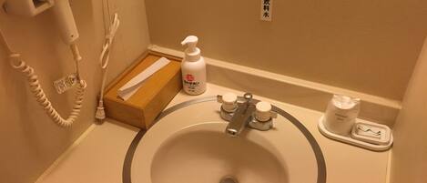 A bathroom with a sink, a hairdryer, a bottle of hand soap, and a tissue box.