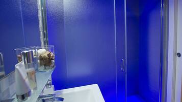 A bathroom with a blue wall, a white sink, and a glass container with a bottle and a bar of soap.