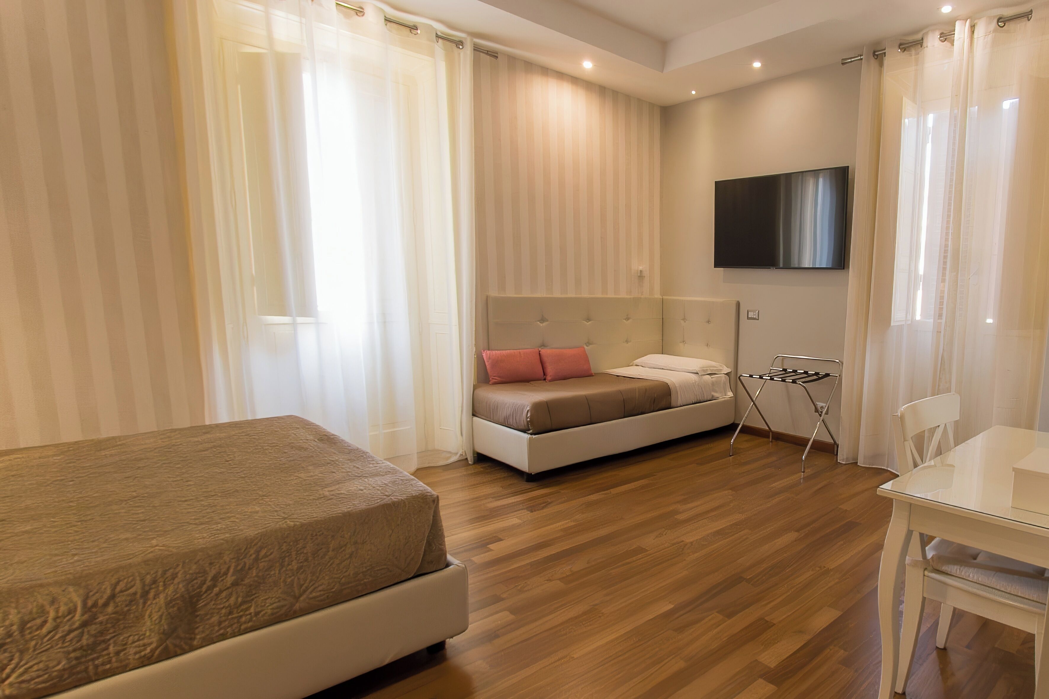 Een moderne hotelkamer met een bed, een klein tafeltje, een stoel, een televisie en een raam met gordijnen.