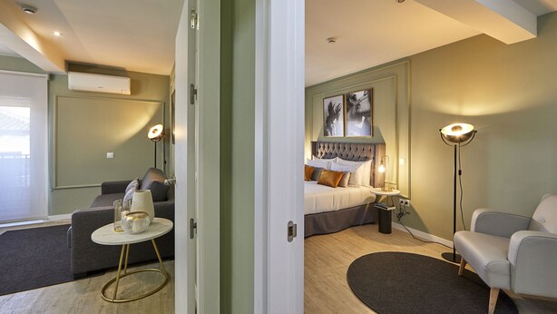 A modern hotel room with a bed, a sofa, a small table, and a floor lamp. - L&H La Latina (Madrid)