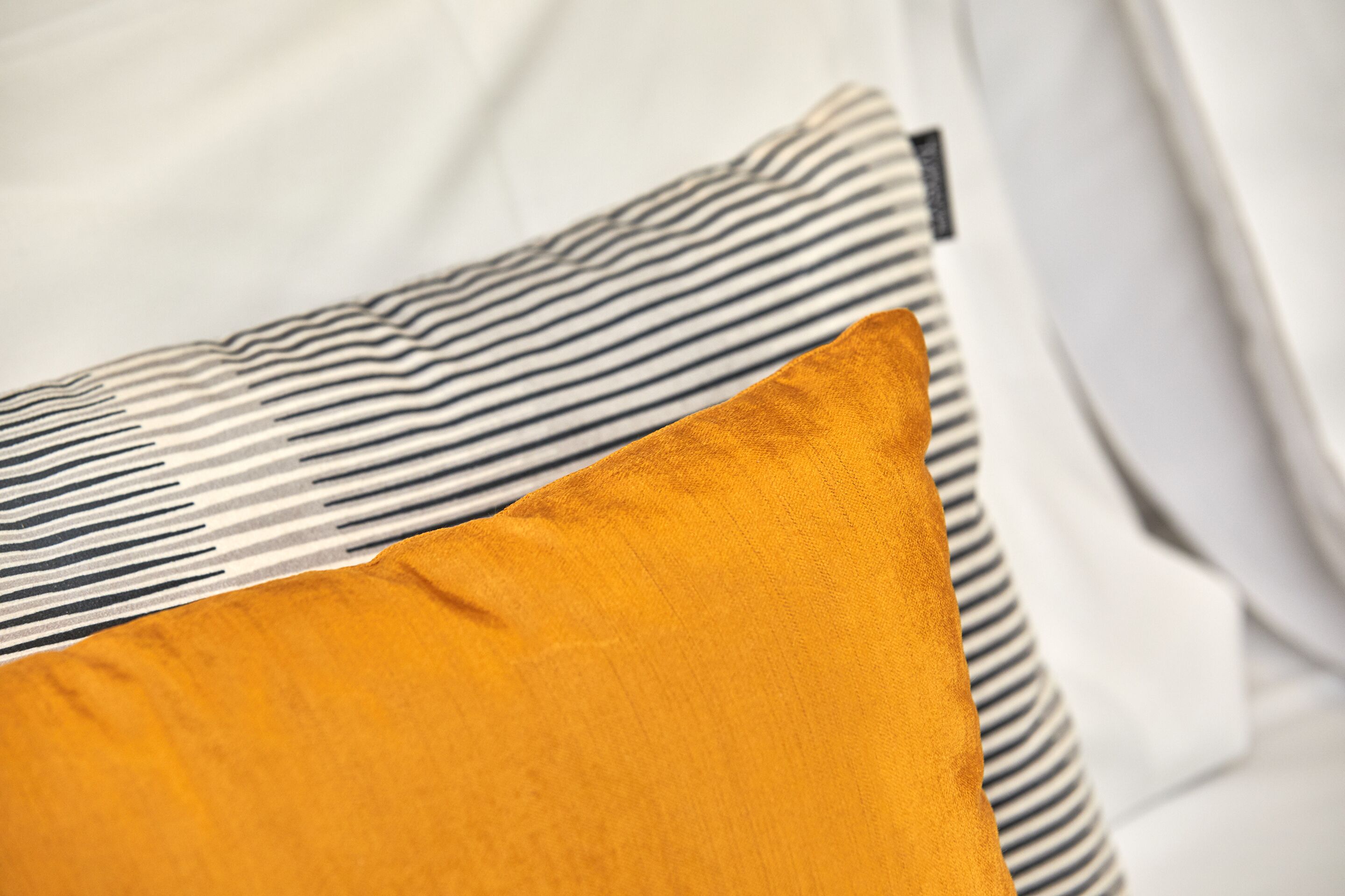 Una cama con un almohadón a rayas y un almohadón de color liso.