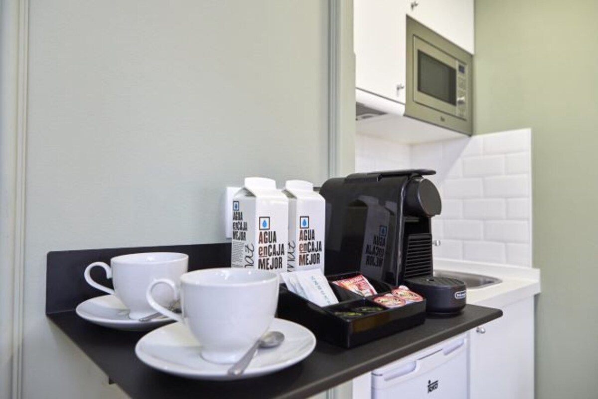 A kitchenette with a coffee maker, milk cartons, and a cup on a counter.