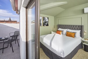 Camera d'albergo con un letto grande, due sedie, un tavolino e vista sulla città.