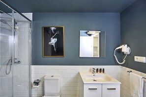 A bathroom with a glass shower enclosure, a white toilet, a sink with a mirror above it, and a hairdryer mounted on the wall. - L&H La Latina (Madrid)