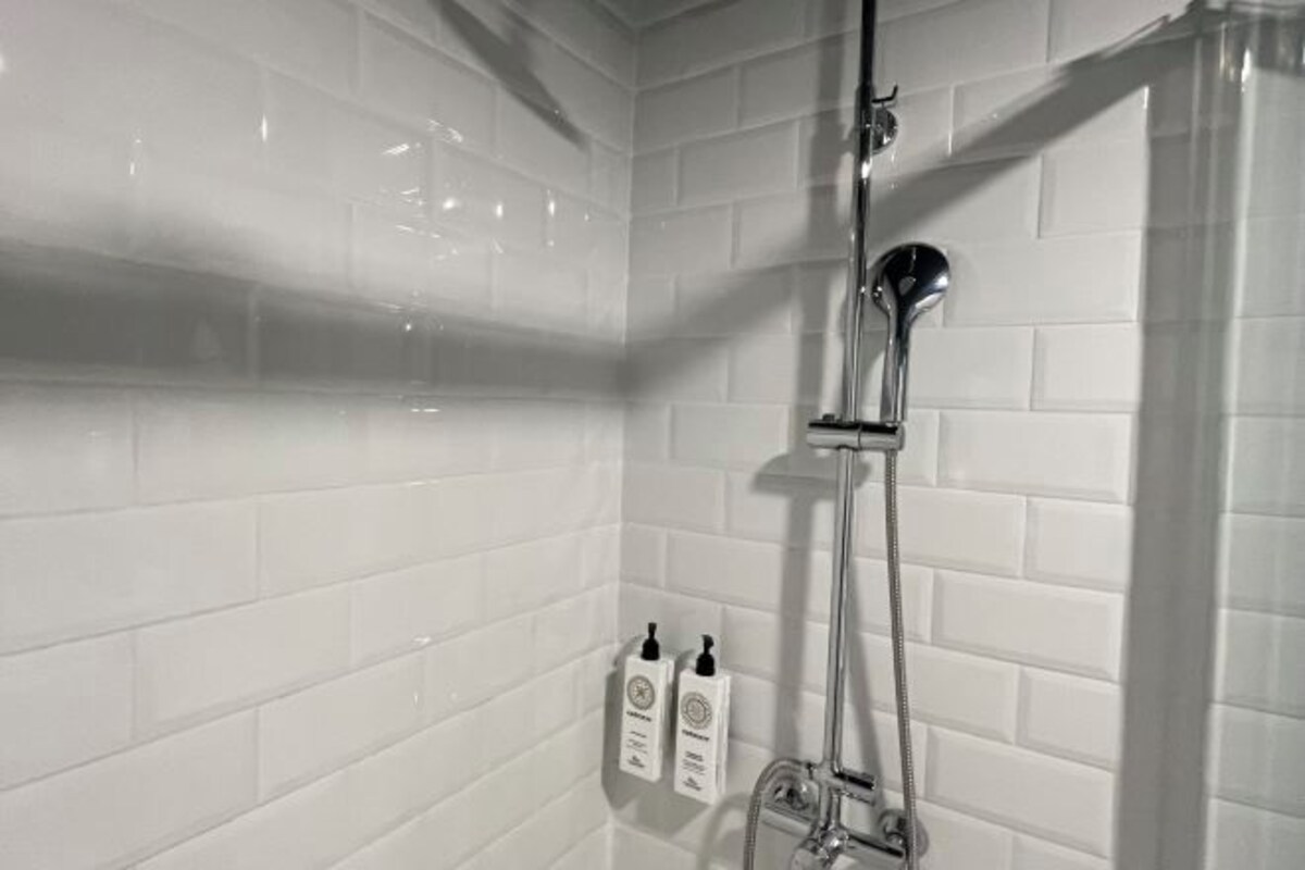 A shower with white tiled walls and a chrome showerhead.