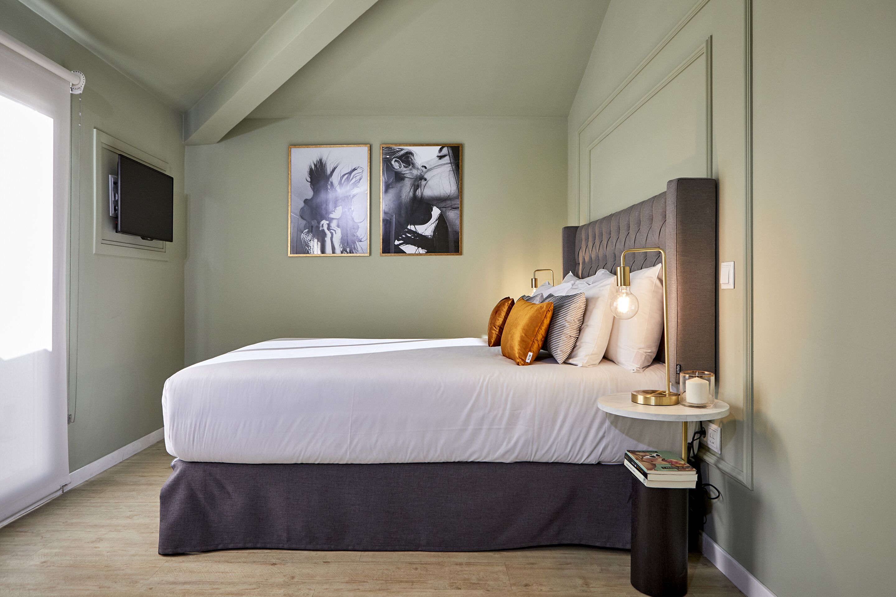 Une chambre avec un grand lit, une table de chevet avec une lampe et deux œuvres d’art encadrées accrochées au mur.