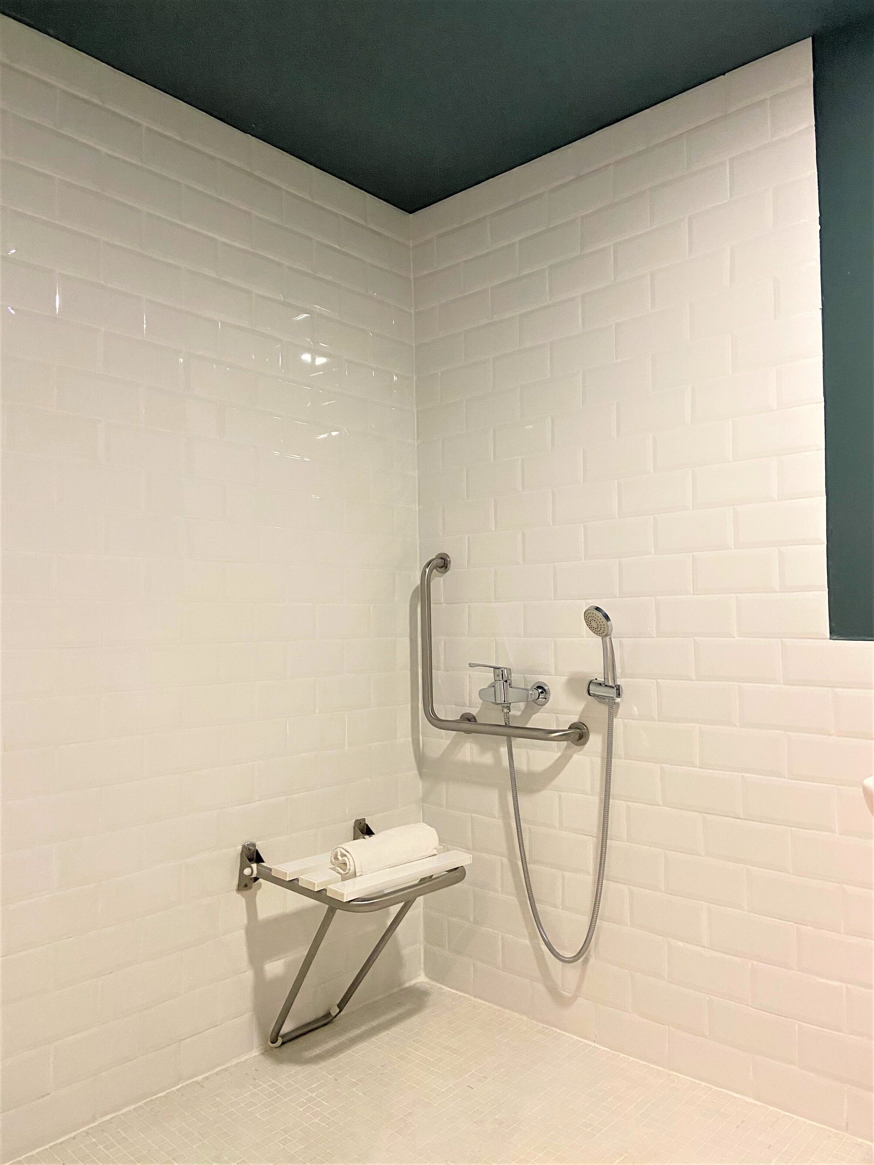 Un área de ducha pequeña con azulejos blancos y un cabezal de ducha de mano.
