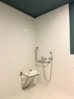 A small, white-tiled shower area with a handheld showerhead and a handheld shower attachment.