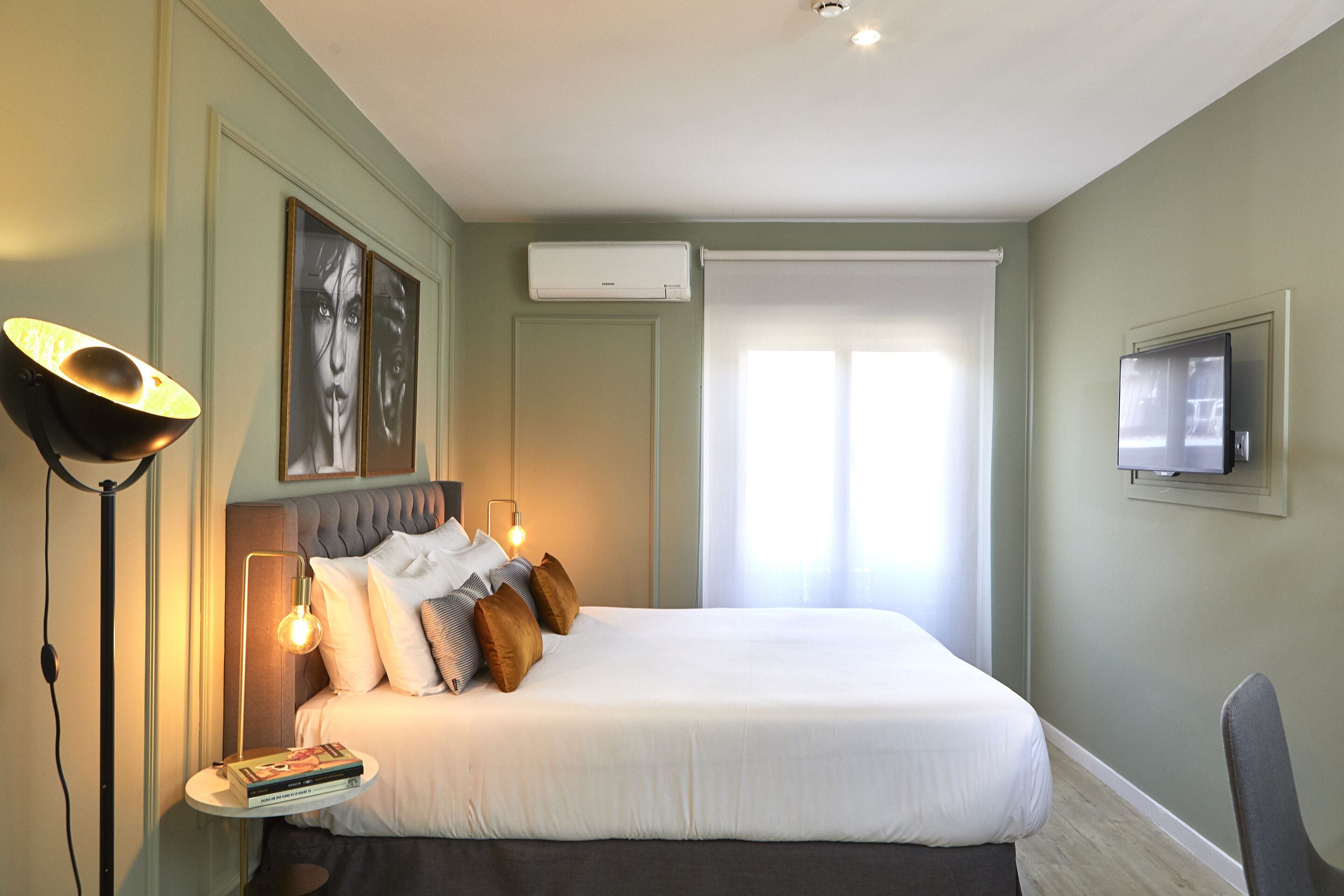 A neatly arranged bedroom with a bed, bedside lamp, and a flat-screen TV on the wall.