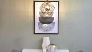 A framed abstract artwork with a geometric design and a hanging light fixture above a white table with a vase and candle. - L&H La Latina (Madrid)