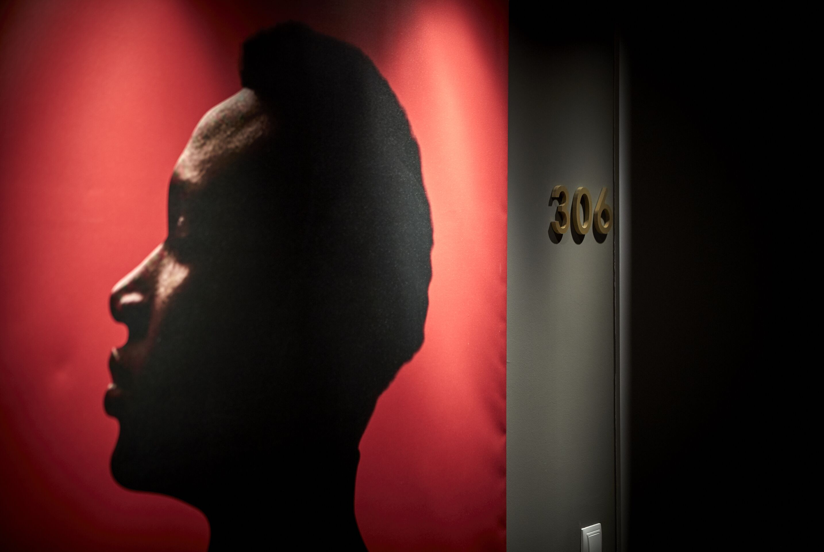 Silueta de una persona contra un fondo rojo, y una puerta con el número 306.