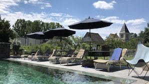 Un espace aménagé au bord de la piscine, avec des chaises longues et des parasols, une piscine à eau claire et un bâtiment en pierre avec une tour en arrière-plan.