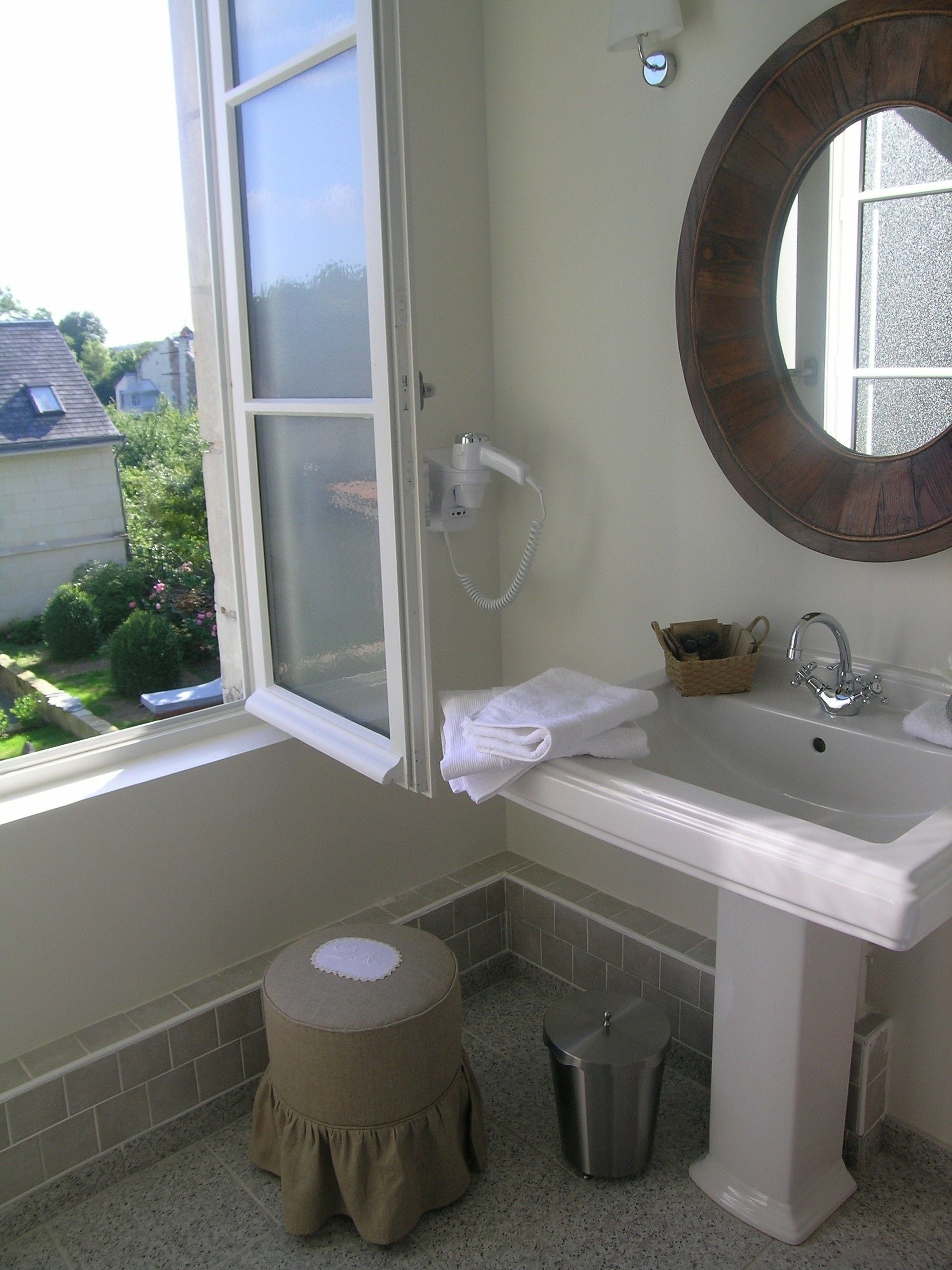 Une salle de bain avec une fenêtre, un lavabo, un miroir et un petit tabouret.
